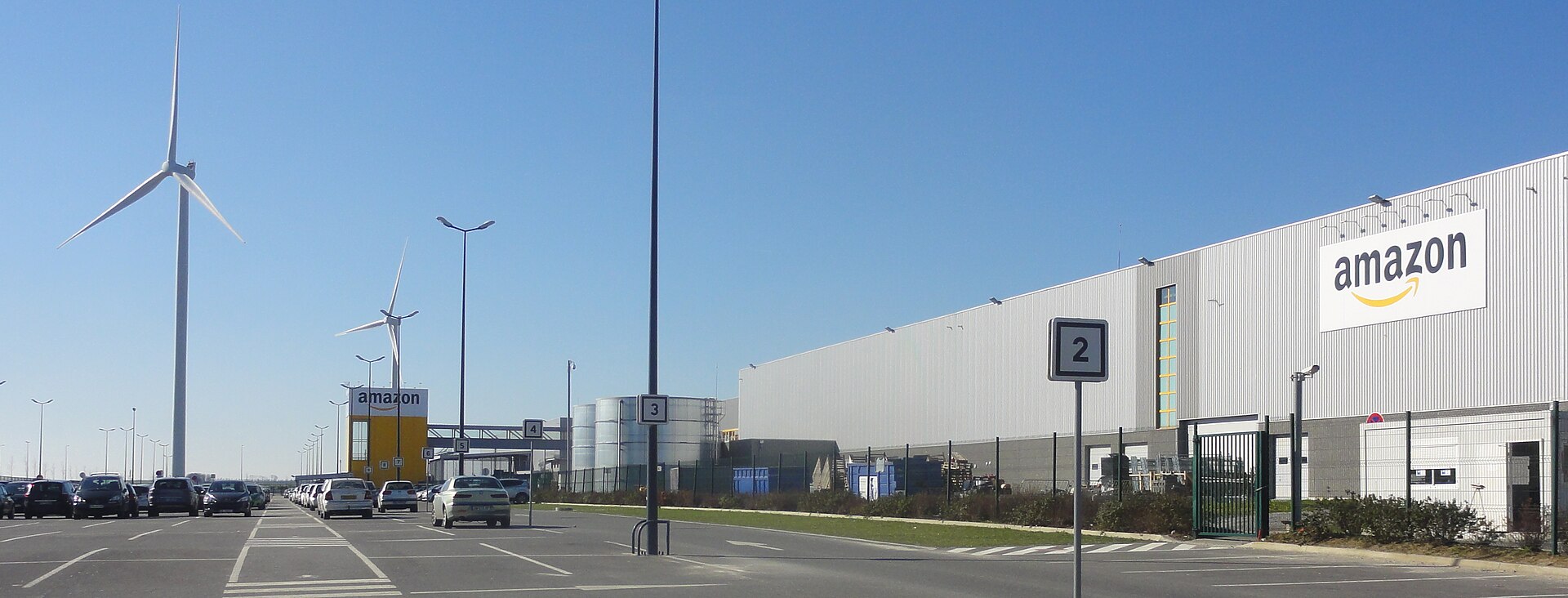 Un entrepôt logistique de grande taille, photographié depuis un parking.